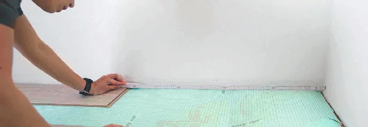 Person verlegt Trittschalldämmung mit Maßband.